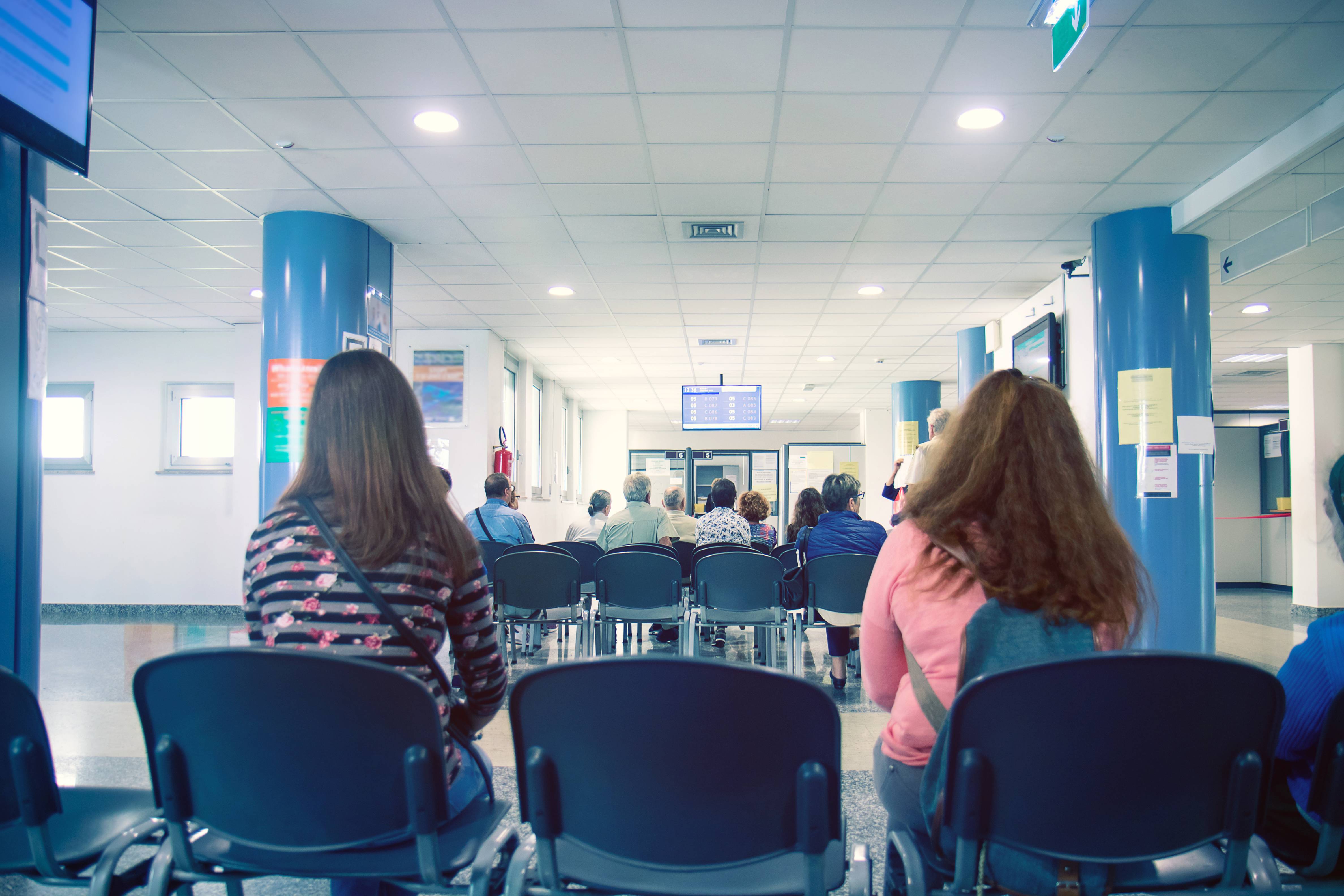 A NHS GP waiting room with patients sat on chairs